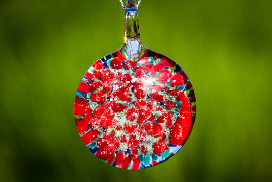 Round glass pendant infused with cremation ashes featuring red and blue marigold petals on a silver chain