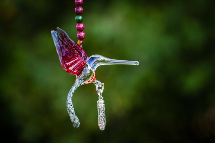 Handmade glass hummingbird pendant with pink and clear glass, pink agate and jade beads, crystal butterfly, and a small silver keepsake urn hanging beneath.