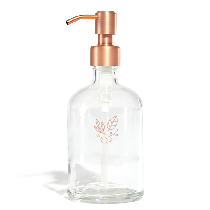 The Grove Co. Refillable Gel Hand Soap Dispenser features a clear glass bottle with a simple two-leaf and small dot design, topped by a metallic copper pump and cap, set against a white background to emphasize sustainability.