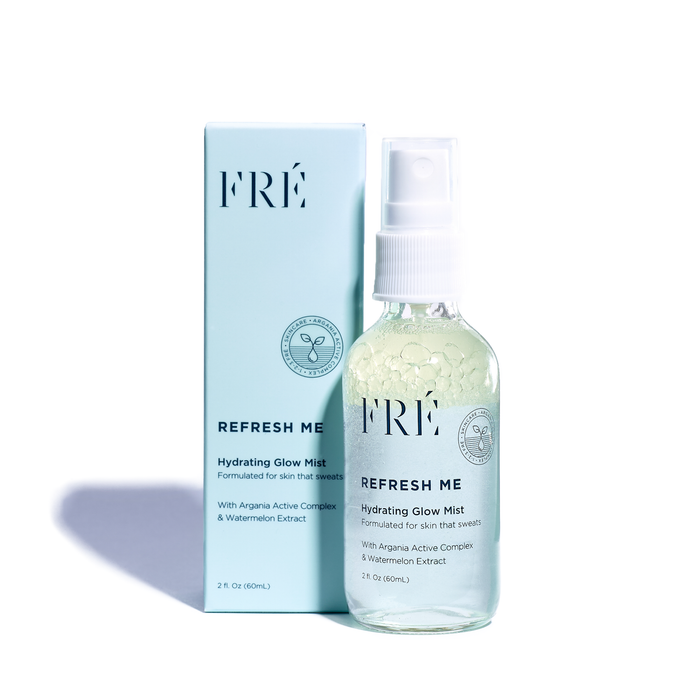 A bottle of FRÉ Skincares REFRESH ME Toning Glow Mist is showcased in front of its light blue packaging. The transparent bottle, with a white nozzle and label, highlights its glow mist benefits and moisturizing ingredients like Argania Active Complex and hyaluronic acid.