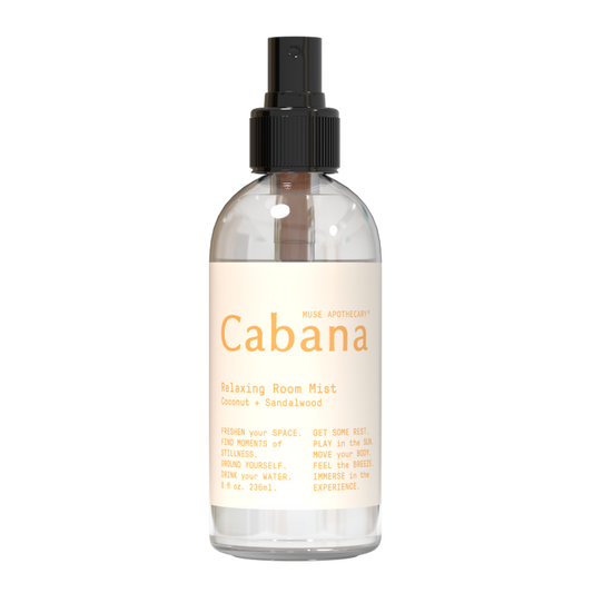 An 8 fl oz (236 ml) clear spray bottle labeled Relaxing Room Mist from Muse Apothecary, featuring a coconut and sandalwood aroma infused with essential oils. It has a black spray nozzle and a beige label that reads, Refresh your space... Feel the breeze.