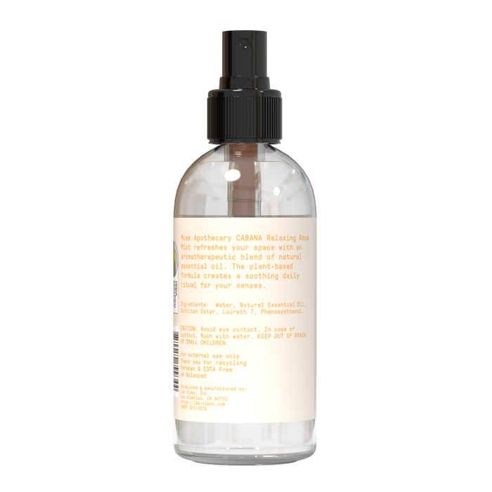 A clear spray bottle, named Relaxing Room Mist by Muse Apothecary, has a black nozzle and provides an aromatherapeutic experience with natural essential oils. The label details ingredients and usage instructions for enhancing your atmosphere.