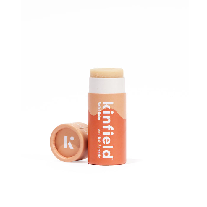 An open Kinfield Relief Balm, with a peach label and description, reveals light beige balm. The cap sits beside it, suggesting a soothing mix of cajeput and colloidal oatmeal for ultimate relief.