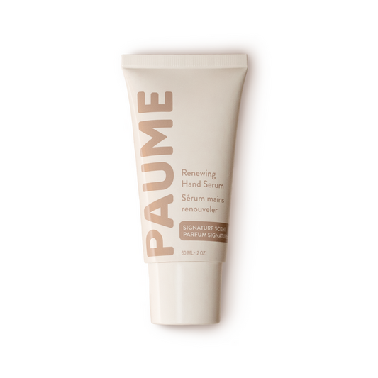 The PAUME Renewing Hand Serum, in a beige tube with white and pink text, is enriched with Hyaluronic Acid. The label, featuring both English and French, emphasizes its Signature Scent. This anti-aging serum rejuvenates skin against a white backdrop.