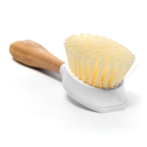 The Grove Co. Replaceable Head Bristle Dish Brush features a bamboo handle and curved white bristles for cleaning dishes and surfaces. Its ergonomic design ensures a comfortable grip, and the replaceable head extends its longevity, all set against a white background.