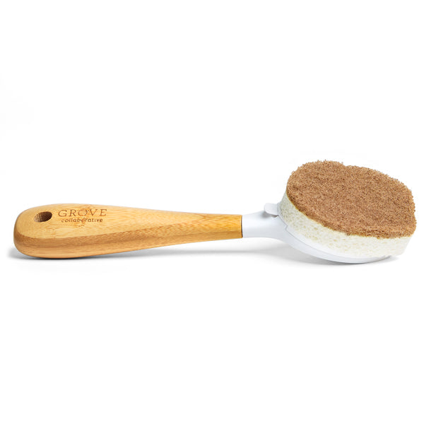 The Grove Co. Replaceable Head Walnut Scrubber Dish Brush has a light wooden handle with a hanging hole and replaceable head. It features a two-tone design: a non-abrasive white layer and brown walnut scrubber for gentle cleaning.