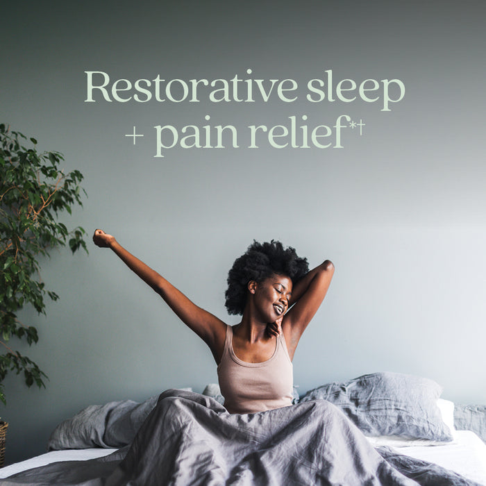 A woman stretches and smiles on a cozy bed, with text above her: Restful Sleep + Pain Relief*. Soft bedding and a plant set a calming mood, highlighting the soothing benefits of New Chapter Restful Sleep and Pain Relief with Melatonin & Ginger.