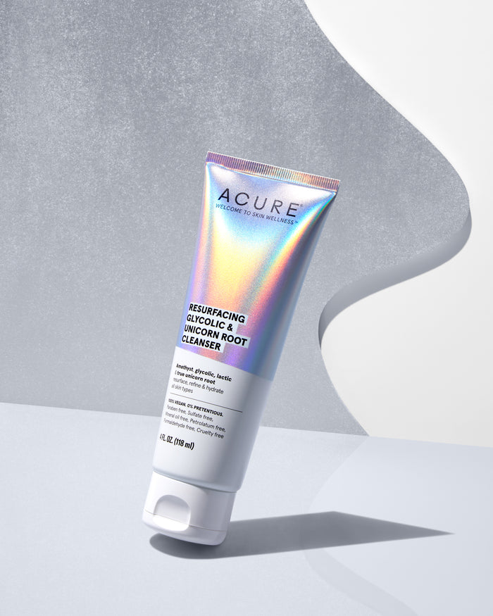 A 4 fl oz (118 ml) holographic tube labeled Acure Resurfacing Glycolic & Unicorn Root Cleanser stands against a gray-white gradient background, casting a gentle left shadow. This cleanser is infused with the magical essence of Unicorn Root.