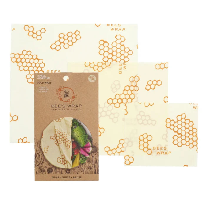 Bee’s Wrap Reusable Beeswax Food Wraps – Assorted 3 Pack, featuring a honeycomb and bee design, are shown beside their packaging, which displays these sustainable wraps in use covering fresh produce.