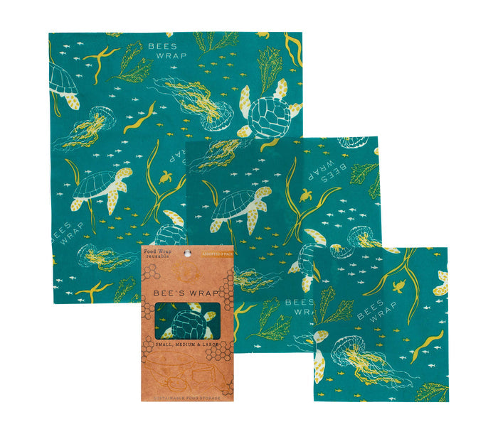 A set of three Assorted Wraps by Bees Wrap, made with organic beeswax, features teal designs of sea turtles, jellyfish, and seaweed. The sustainable food storage set comes in small, medium, and large sizes and is packaged in eco-friendly cardboard.