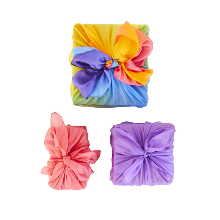 Three gift boxes wrapped in Sarahs Silks Reusable Gift Wrap Furoshiki Set with intricate knots: rainbow, pink, and purple patterns, each adorned with unique bows. Ideal for sustainable gift-giving against a white backdrop.