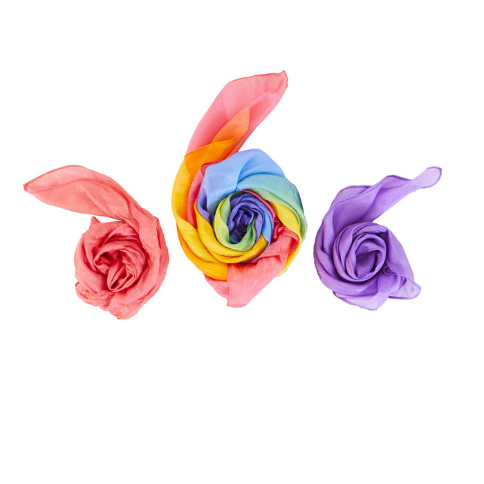 Three fabric roses made from Sarahs Silks Reusable Gift Wrap Furoshiki rest against a white background: pink on the left, rainbow in the center, and purple on the right. These intricately tied mulberry silk petals resemble blooming flowers—ideal for eco-friendly gifting.