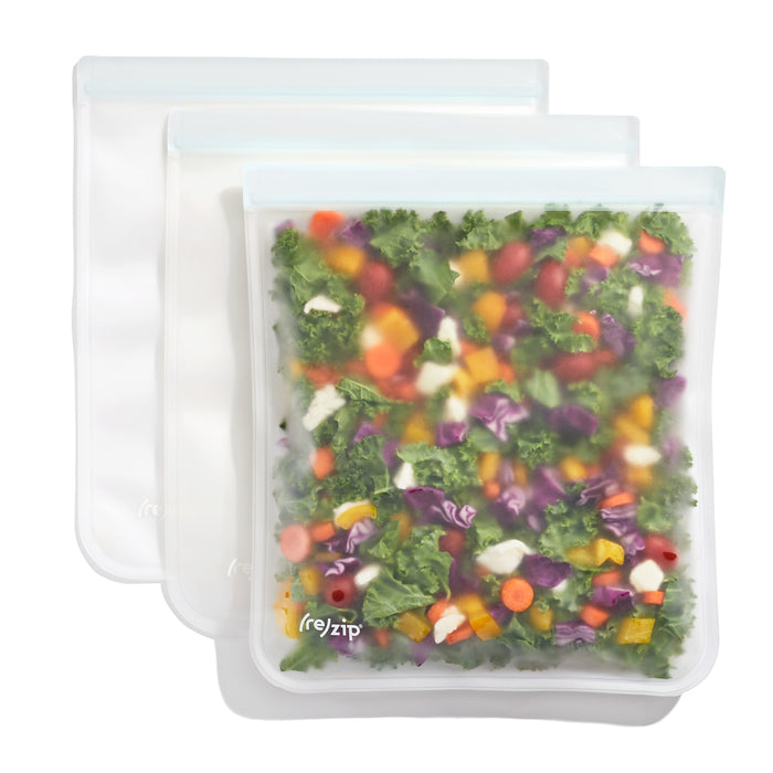 Three (re)zip Reusable Leakproof Gallon Bags are displayed: the front transparent bag holds chopped colorful vegetables, while two empty bags overlap behind it.