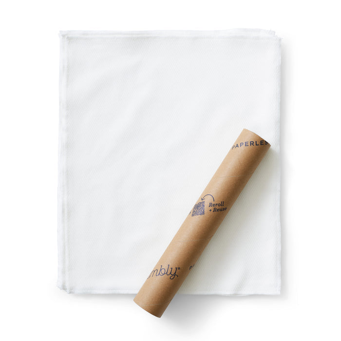 A brown cylindrical cardboard tube labeled Reroll + Reuse and Esembly Baby rests diagonally on a folded piece of 100% organic cotton with a textured surface and stitched edges. This eco-friendly product offers a sustainable alternative to traditional paper towels.