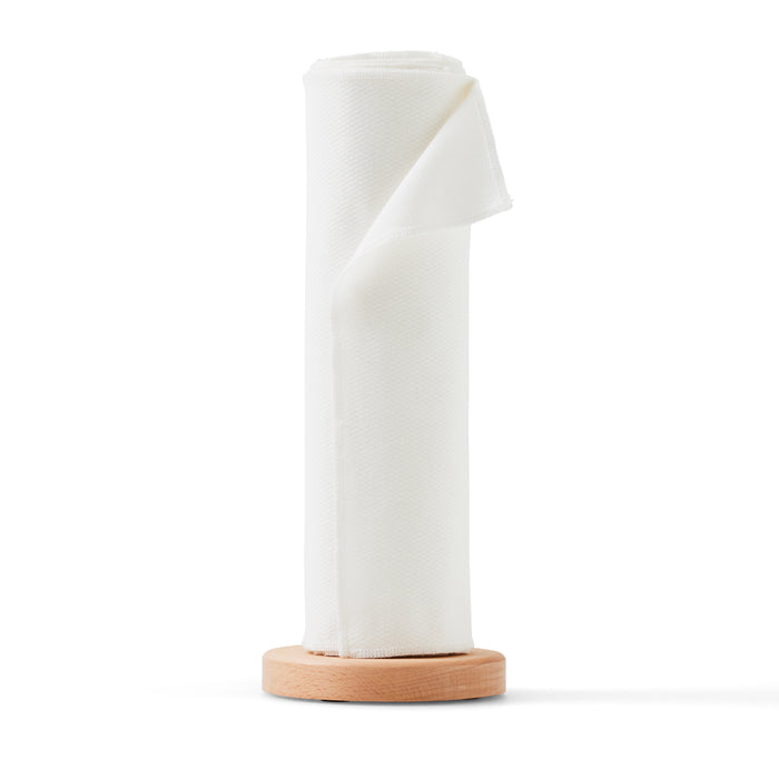 A roll of reusable paper towels from Esembly Baby, crafted from certified 100% unbleached organic cotton, stands upright on a round, light wooden base against a plain white background. The fabric is neatly rolled with a portion slightly unwrapped at the top, embodying eco-friendly cleaning solutions.
