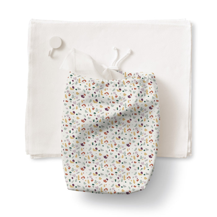 The Esembly Baby 100% Organic, Unbleached Reusable Paper Towel Set includes 12 towels, a roll, toss bag, and hook—shown here with a towel beneath the included colorful toss bag featuring an abstract speckled pattern.