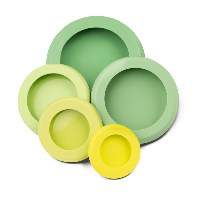 Five nested Reusable Silicone Food Savers from Food Huggers, in green and yellow, offer space-saving storage. Arranged concentrically on a white background, they showcase glossy surfaces that highlight innovation and embody the essence of preserving fresh produce.