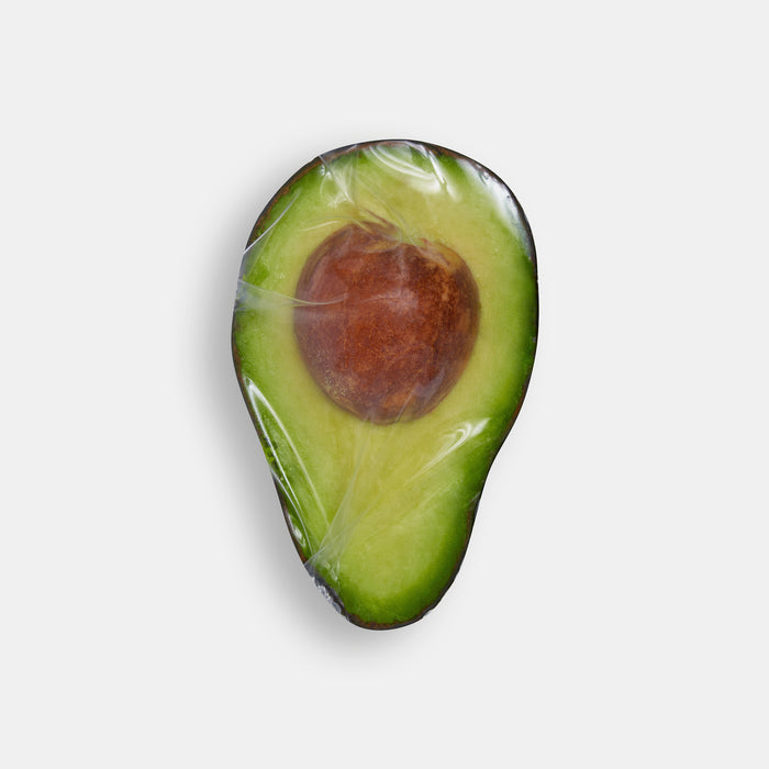 An avocado half with its seed visible is elegantly wrapped in a W&P Reusable Silicone Stretch Wrap, set against a plain white background.