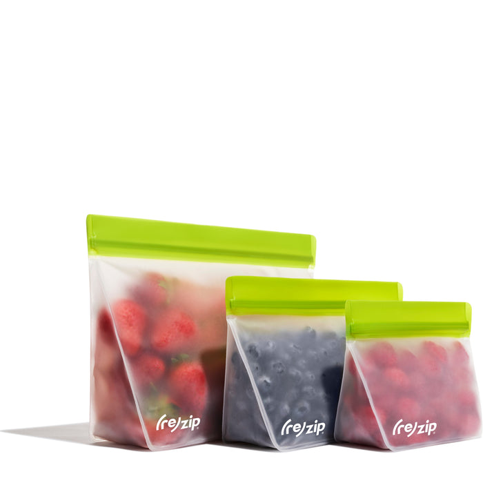 Three (re)zip Reusable Stand-Up Bags made of food-grade PEVA, each with a green zip, hold strawberries, blueberries, and raspberries. Semi-transparent and leakproof, they are displayed in a row.