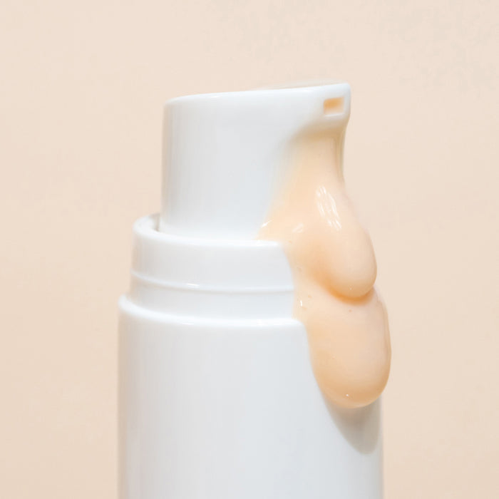 Close-up of a white pump bottle dispensing a creamy, peach-colored liquid, featuring Wildcrafts Revive Bio-Retinol Face Serum—a plant-based retinol alternative for ultimate skin revitalization—set against a plain beige background.