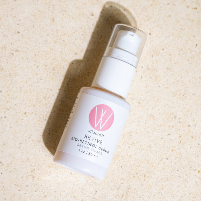 A white bottle of Wildcrafts Revive Bio-Retinol Face Serum with a pink logo sits on a light beige surface, featuring a plant-based retinol alternative in a 1 oz (30 ml) pump dispenser for skin revitalization.