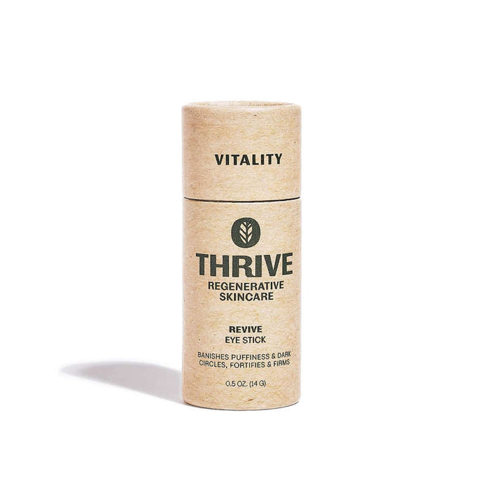 The Revive Eye Stick from Thrive Natural Care, in a cylindrical cardboard container, boosts skin elasticity. Minimalist beige packaging with bold black text emphasizes the vitality-boosting power of Thrives super-plants.