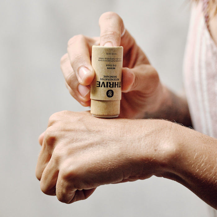 Someone is using the Thrive Natural Care Revive Eye Stick on their hand, highlighting its sleek design and smooth application. Enriched with Thrive super-plants, it provides nourishing protection while offering bakuchiol benefits for rejuvenation.