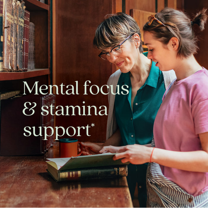 Two women stand by a bookshelf, reading an open book. One holds a coffee mug. Text: Mental focus, stamina, and stress support* with adaptogen Rhodiola—New Chapter Rhodiola Force 300 Mental Health & Stamina.