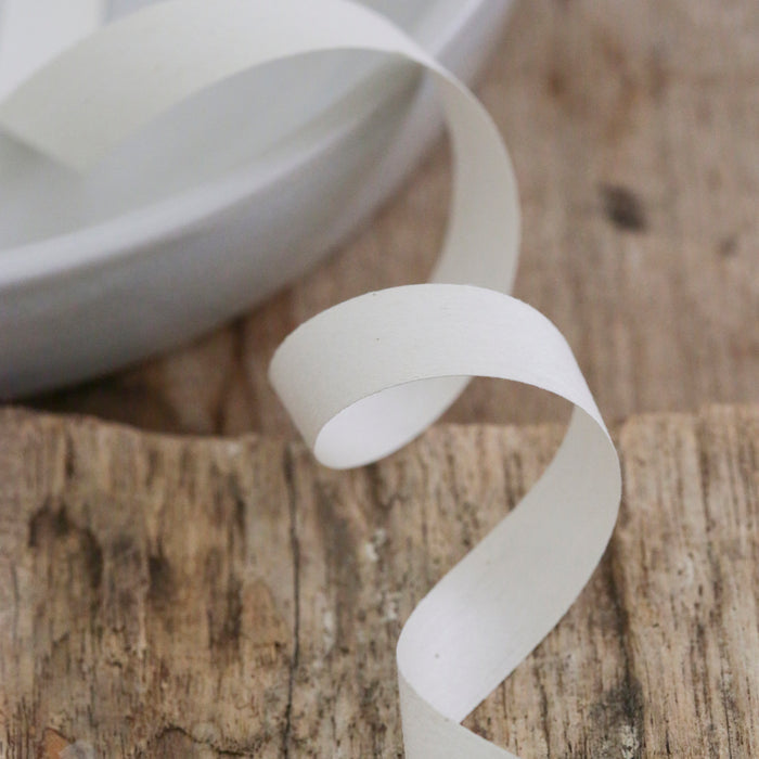 A sustainable ribbon from Waterleaf Paper Company elegantly drapes over a weathered wooden surface, partially resting on a white plate in the background.