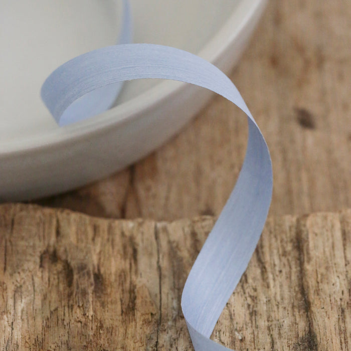 A light blue Ribbon from Waterleaf Paper Company is elegantly curled on a rustic wooden surface, with part of it placed in a round, light-colored bowl in the background.