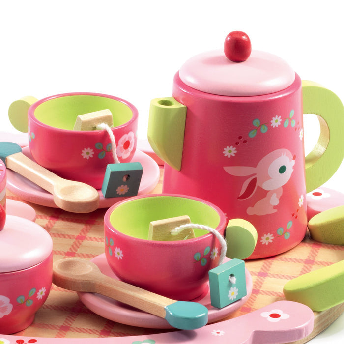 The DJECO Role Play Lili Rose’s Tea Party Set, made from 100% FSC® Certified wood, is a non-toxic pink toy featuring floral and bunny designs. It includes a teapot with a red knob, cups with green interiors, wooden spoons, teabags, all on a plaid-patterned tray.