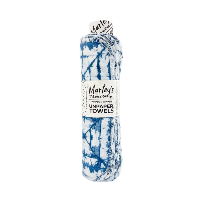 The Rolled Unpaper® Towels by Marleys Monsters feature a blue and white tie-dye pattern. These eco-friendly, reusable cloths are rolled up and secured with a label displaying the brands logo.
