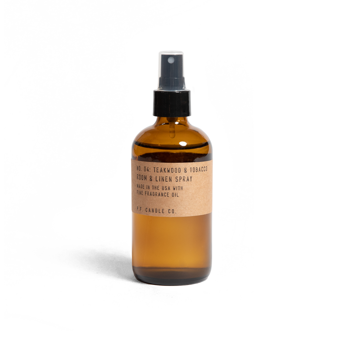 A brown glass spray bottle labeled No. 04: Teakwood & Tobacco Room & Linen Spray by P.F. Candle Co., crafted in the USA with fine fragrance oil for a rich woody scent, features a sleek design with a black spray nozzle.