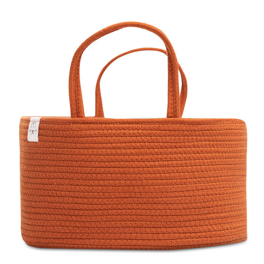 The Natemia Rope Diaper Caddy, featuring a rope-like pattern and rectangular shape, is made from GOTS Certified Organic Cotton. Its orange hue, dual handles, and small white tag make it the perfect nursery storage solution for holding baby nappies.
