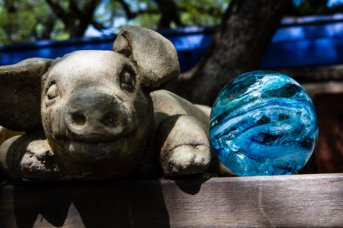 Teal and turquoise rope glass orb infused with cremation ashes resting beside a stone pig statue