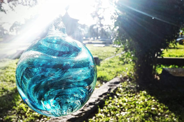 Blue teal rope glass orb with swirling patterns suspended outdoors in bright sunlight