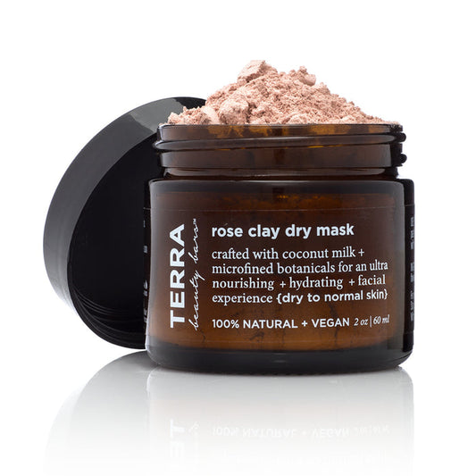An open jar of Terra Beauty Bars Rose Coconut Dry Facial Clay Mask showcases its pink powder. The label emphasizes 100% natural hydrating vegan botanicals and coconut milk, ideal for a rejuvenating facial experience on dry to normal skin.