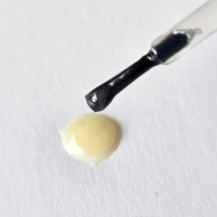 A close-up of a Naturally London Rosehip Hydrating Cuticle Oil with Willow Bark brush above a small drop on a white surface, perfect for achieving healthy nails.