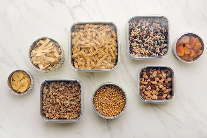 U-Konserves Round Container Large displays fusilli pasta, dried fruit, mixed beans, popcorn kernels, mixed nuts, granola, and banana chips on a marble surface. This plastic-free setup offers a sustainable pantry organization solution.