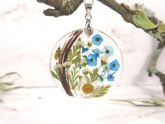 Round crystal resin pendant encasing dried flowers and a lock of hair, suspended from a silver chain.