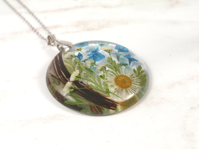 Round crystal resin pendant filled with blue blossoms and a white daisy inside.