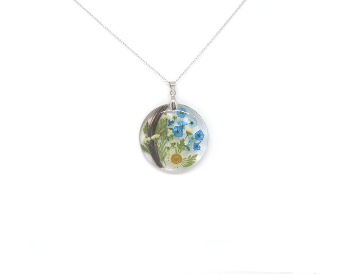 Round crystal resin pendant filled with pressed wildflowers in blue and yellow, on a silver chain.
