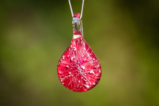 Red ruby slippers inspired glass pendant with white splash pattern on a silver chain, containing cremation ashes.