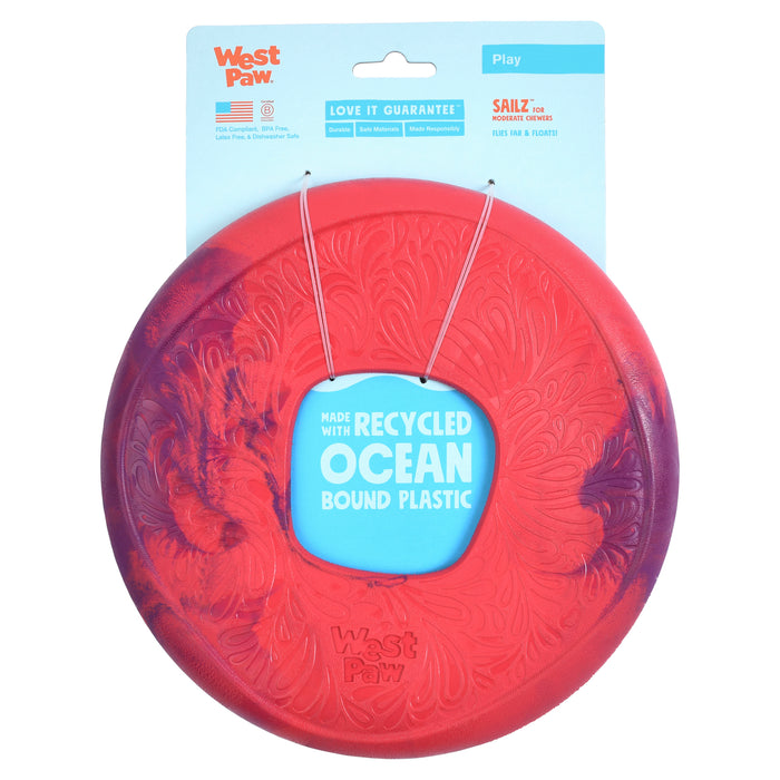 Introducing West Paws Sailz® Fetch Flyer, a durable and lightweight red and purple dog toy crafted from recycled ocean-bound plastic. Perfect for the beach, it comes in blue packaging with a handle, featuring logos and sustainability info.