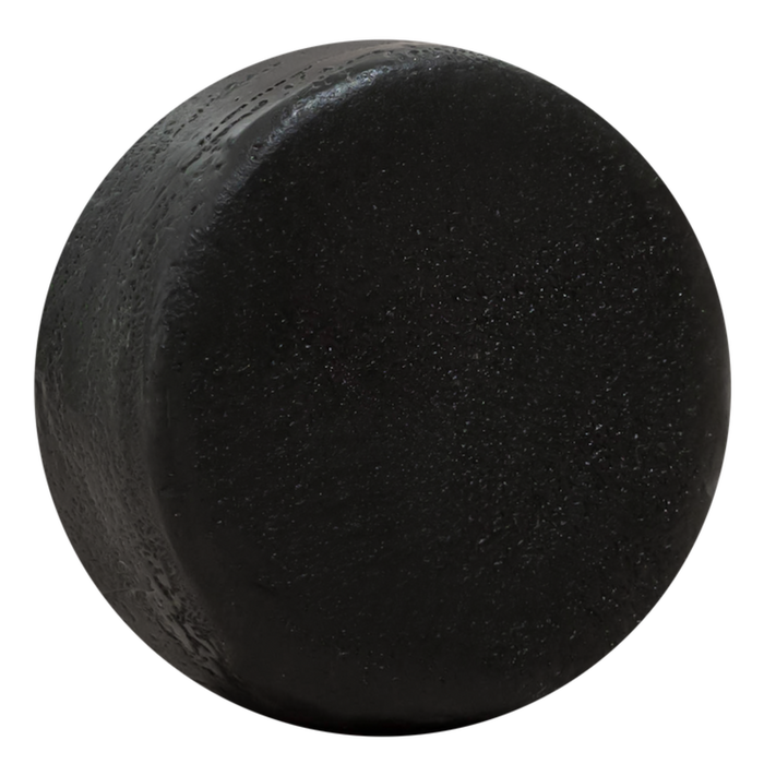 A close-up of a black hockey puck with a textured surface, set against white—its smooth finish evokes the feel after using Good Juju Body & Home’s Scalp Care Conditioner Bar.