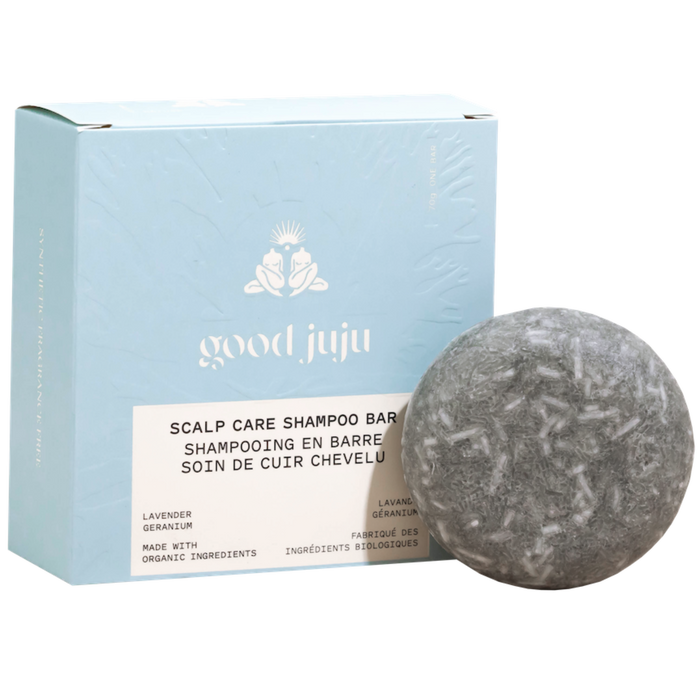 A round grey Scalp Care Conditioner Bar by Good Juju Body & Home sits before a light blue box with white lettering. Made with organic ingredients, it naturally conditions hair and helps relieve dandruff with lavender and geranium.
