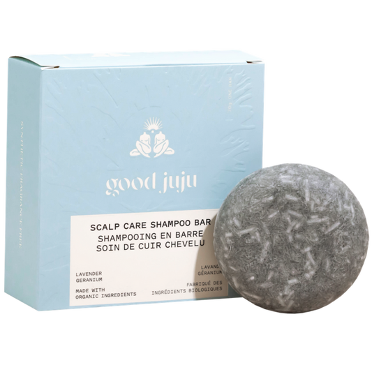 A round grey Scalp Care Conditioner Bar by Good Juju Body & Home sits before a light blue box with white lettering. Made with organic ingredients, it naturally conditions hair and helps relieve dandruff with lavender and geranium.