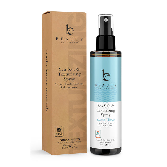 A bottle of Beauty by Earths Sea Salt Spray Hair Texturizer, labeled Ocean Waves, is displayed with its matching cardboard packaging. The black bottle with a blue label and spray nozzle helps you effortlessly achieve beachy hair texture.