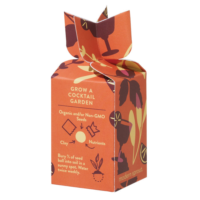 The Seed Bomb - Grow Good Times by Modern Sprout is a charming orange box with botanical designs and organic seed bombs. Instructions advise planting ⅔ of the seed ball in sunny soil and watering twice weekly. The folded top showcases leaves and cocktail glass motifs, hinting at future herbal treats.