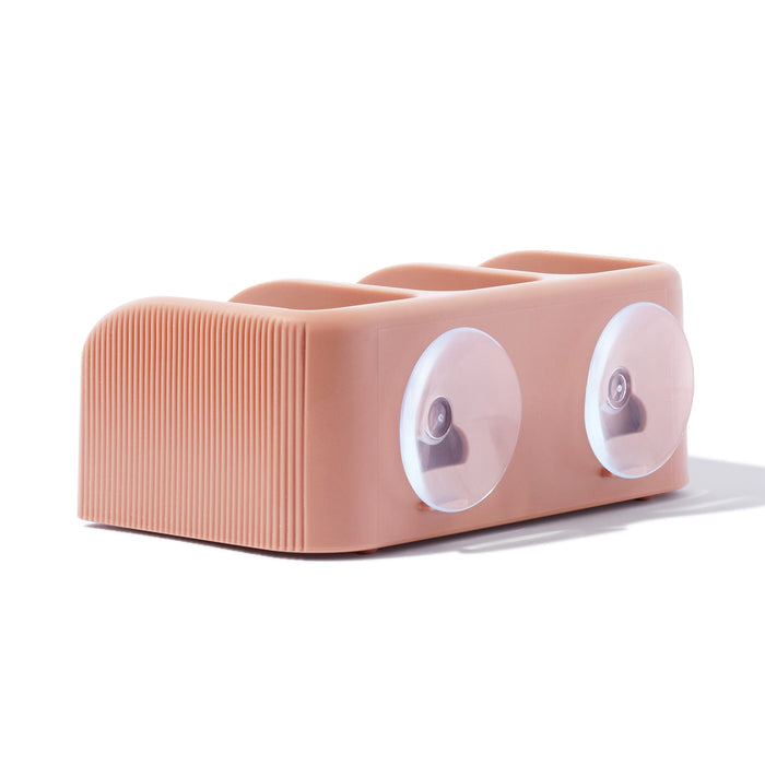 The Kitsch Self Draining Soap Dish is a peach-colored, rectangular silicone organizer with ribbed sides and three top compartments. It includes two clear suction cups for support and promotes the Bottle-Free Beauty lifestyle.